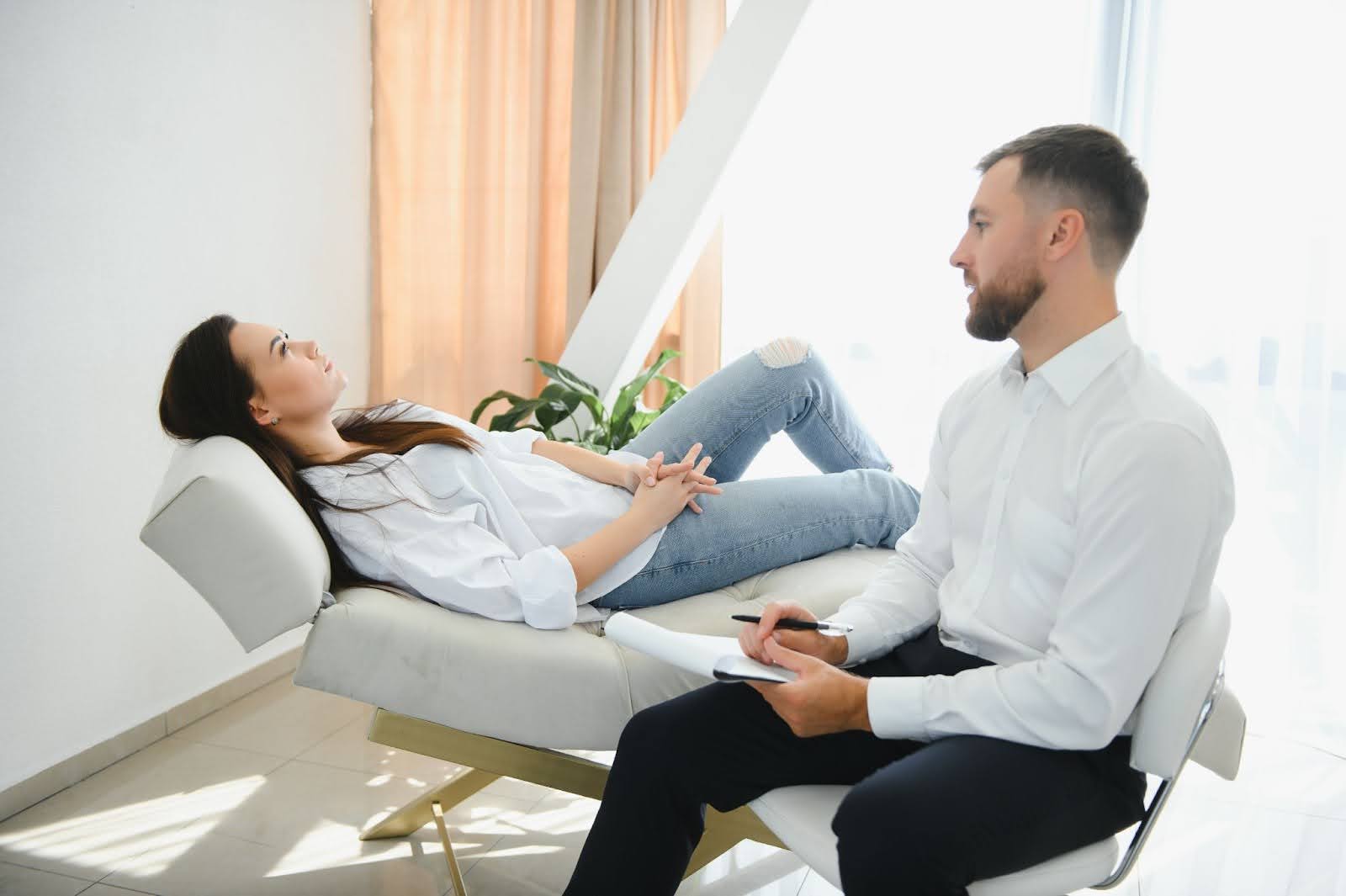 Woman lying on the couch while receiving therapy for mental health from a male doctor.