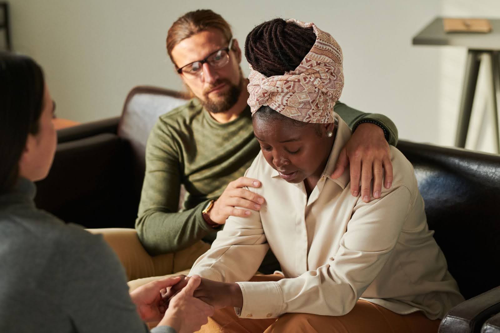 Couple receiving grief counseling, with husband gently supporting his wife as they speak with a therapist.