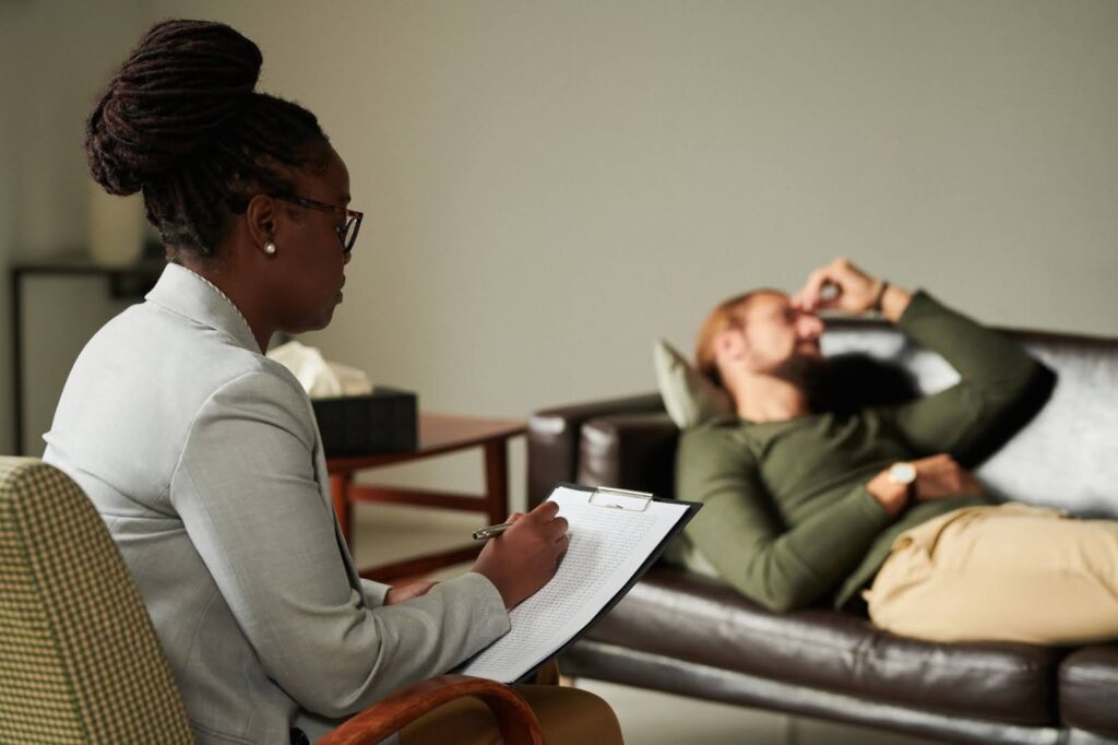A psychologist is taking notes during individual therapy with a patient lying on the couch.