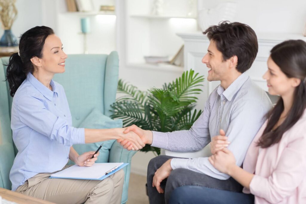 A female psychologist shakes hands with a relieved couple at the end of a successful counseling session.