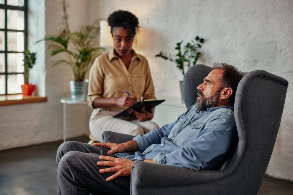 Alt-text: An African female therapist holding a chart provides individual therapy to a mid-adult male client.