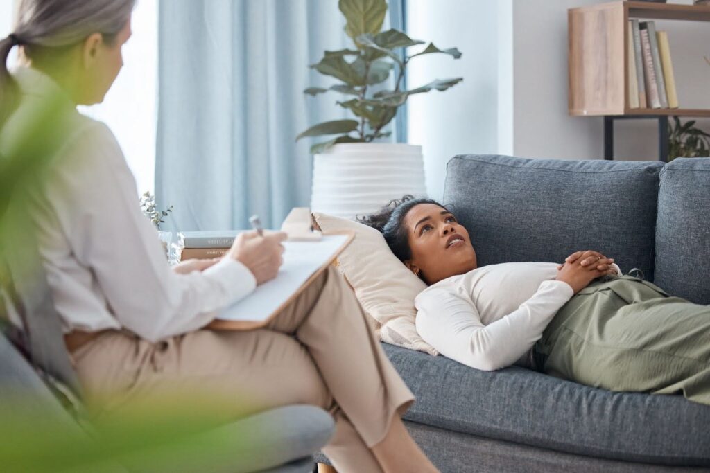 A woman shares her story with a therapist while lying on a couch during a session.