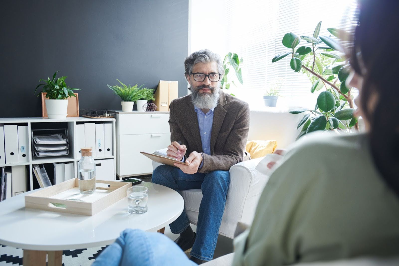 A therapist with pen and paper in hand looks at his patient during a session.