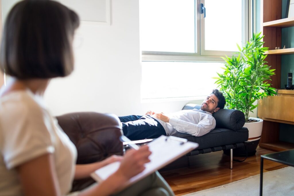A patient looks at his psychotherapist while lying on a daybed during a session.